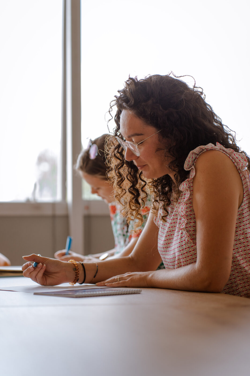 jeune femme qui écrit sur une feuille accourdée à un bureau avec d'autres personnes qui suivent une formation