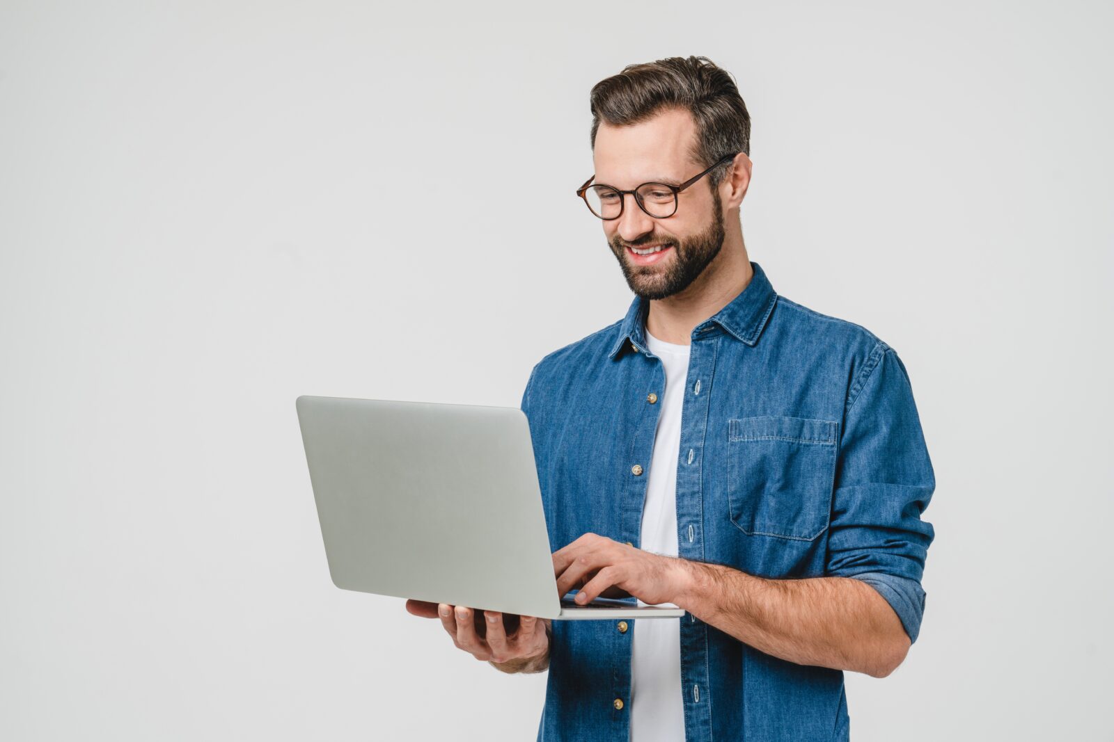 homme souriant tenant un ordinateur vêtu d'une chemise en jean bleu et d'un t shirt blanc, il porte des lunettes